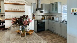 A kitchen with wooden shelves, a clock, cabinets, a stove, and a sink.