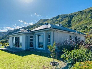 Una casa moderna con un patio amplio, un jardín pequeño y montañas al fondo.