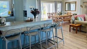 A kitchen with a bar area, wooden dining table, and a sofa in a bright living room.