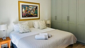 A bedroom with a bed, pillows, a nightstand, a lamp, a painting, and a wardrobe.