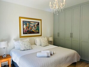 Un dormitorio con cama, almohadas, mesita de noche, lámpara, un cuadro y armario.