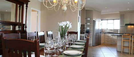 A dining area with a chandelier, a table set for six, and a kitchen in the background.