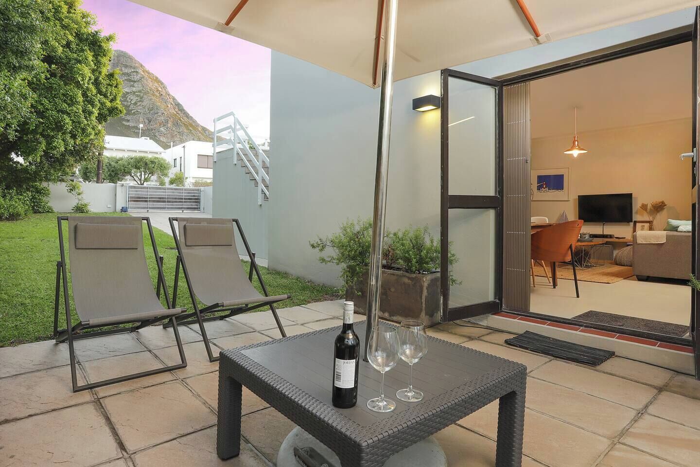 An outdoor patio with a table, chairs, and a bottle of wine.