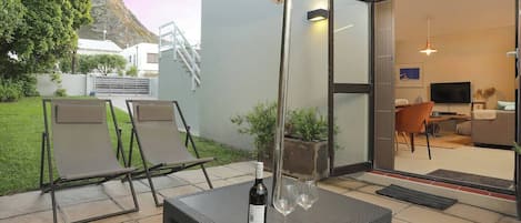 An outdoor patio with a table, chairs, and a bottle of wine.