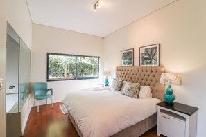 A bedroom with a large bed, a chair, a nightstand, and a window with a view of trees.