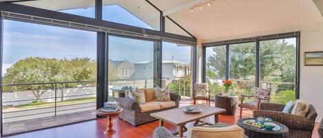 A spacious balcony with wicker furniture, large windows, and a view of the surrounding area.