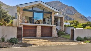 A modern two-story house with a balcony, stone facade, and a garage. - Seaside Symphony Villa | Walking distance to Grotto Beach (Hermanus)
