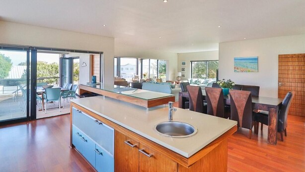 A modern kitchen with a central island, dining area with chairs, and large windows offering views. - Seaside Symphony Villa | Walking distance to Grotto Beach (Hermanus)