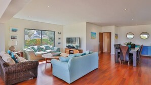 A spacious living area with a sofa, a television, and a dining table with chairs. - Seaside Symphony Villa | Walking distance to Grotto Beach (Hermanus)