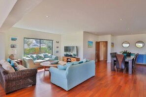 Uma sala de estar ampla com sofá, televisão e mesa de jantar com cadeiras.