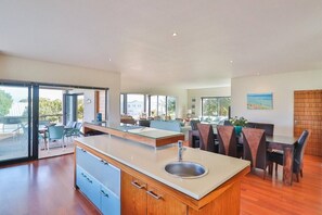 A modern kitchen with a central island, dining area with chairs, and large windows offering views.