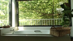 Un baño con bañera, una ventana que da a árboles y una cesta de mimbre en la encimera.