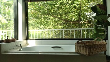 A bathroom with a bathtub, a window with a view of trees, and a wicker basket on the counter.
