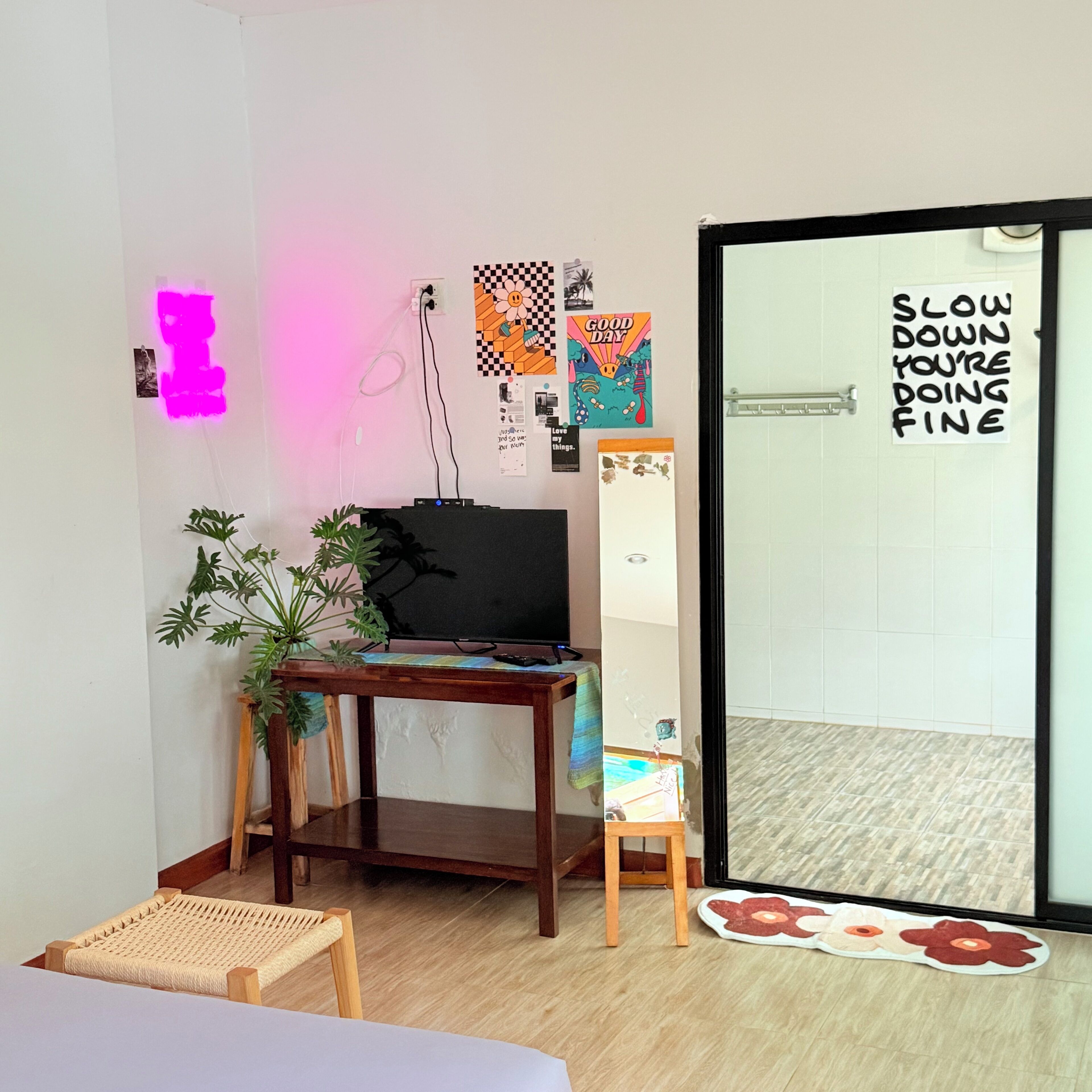 Ένα δωμάτιο με ένα κρεβάτι, ένα γραφείο με έναν υπολογιστή, ένα μικρό φυτό και μια πόρτα με μια πινακίδα.