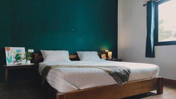A neatly made bed with white linens and a patterned throw, a bedside table with a lamp, and a wall-mounted painting.