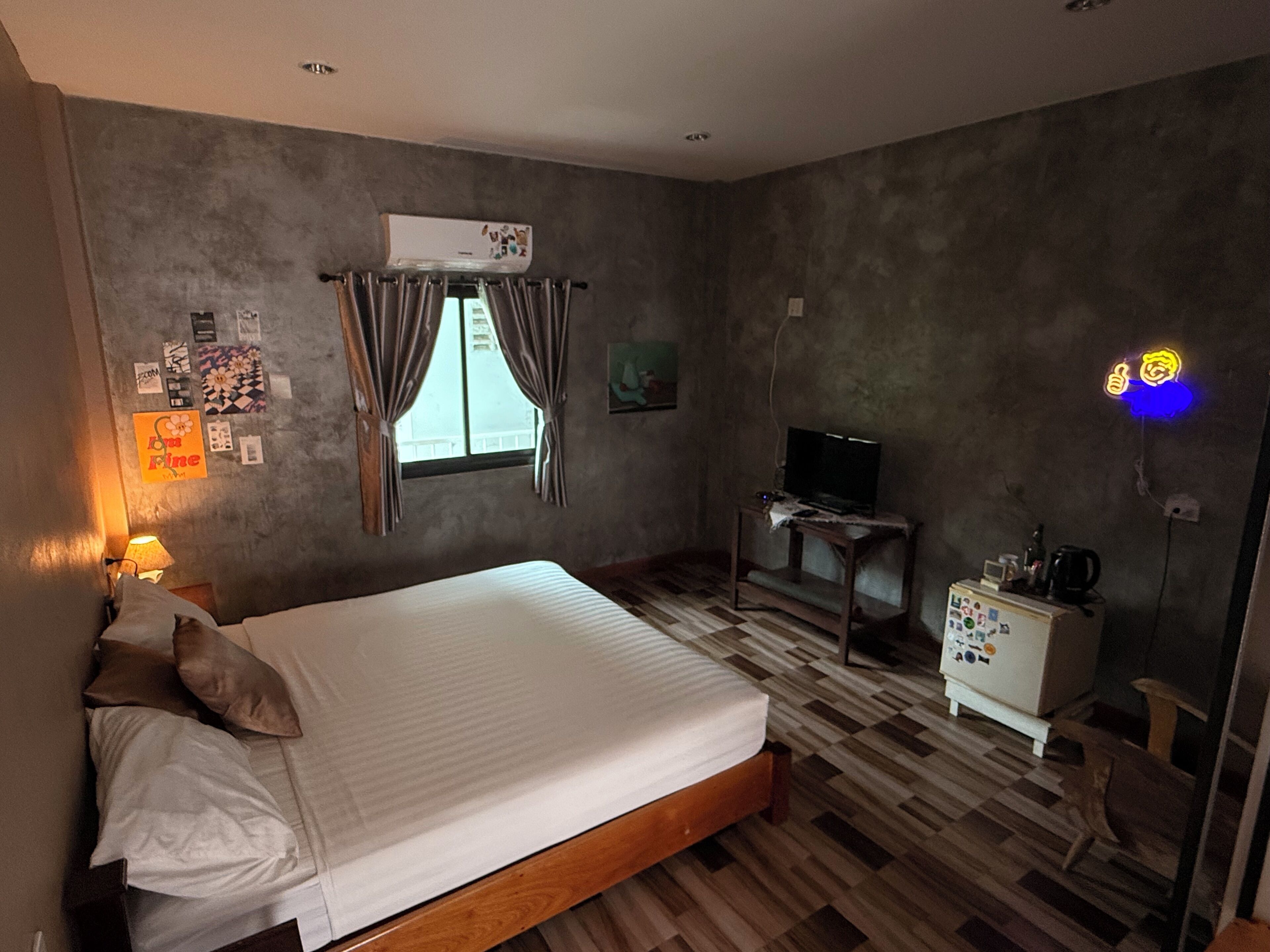 Un dormitorio con cama, escritorio, televisor y un letrero de neón.