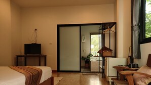 Habitación de hotel con cama, televisor sobre un pedestal, escritorio con silla, ventana y puerta corredera hacia un baño.