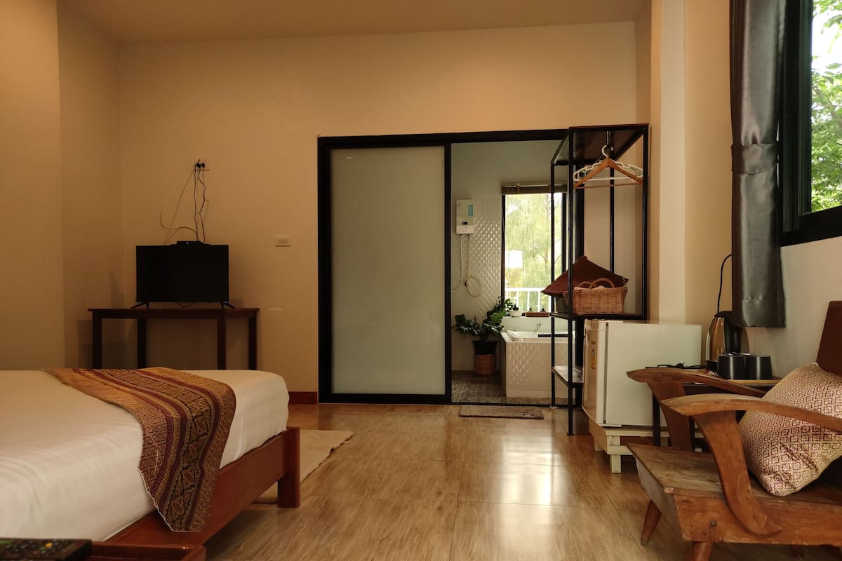 A hotel room with a bed, a TV on a stand, a desk with a chair, a window, and a sliding door leading to a bathroom.