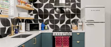 A modern kitchen with a black and white geometric backsplash, a stainless steel range hood, a white Galanz refrigerator, and teal cabinetry.