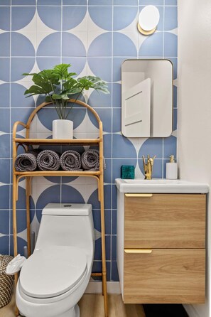 A bathroom with a toilet, a shelf with rolled towels, a potted plant, a mirror, and a cabinet with drawers. - Luxe Studio Retreat - Close to DT & UT Austin (Austin)