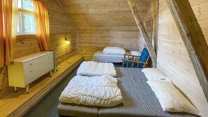 A wooden cabin room with two beds, a small desk, and a window with curtains.