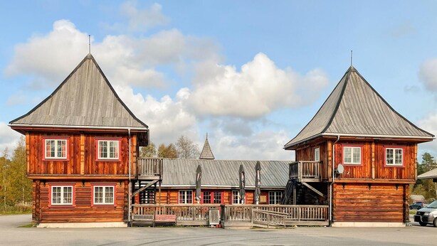 A wooden building with two prominent towers and a central section with a staircase.