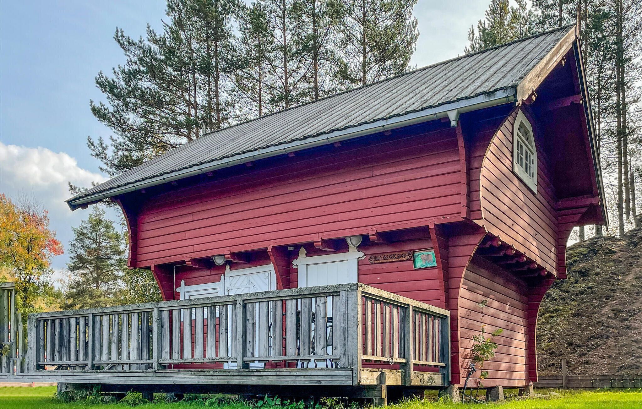 A red wooden cabin with a porch, surrounded by trees.