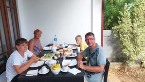 Un groupe de personnes est assis autour d’une table, devant différents plats, des tasses et une bouteille d’eau.