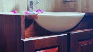 Une salle de bain avec un meuble-lavabo en bois, un lavabo blanc et une plante en pot posée sur l’étagère au-dessus du miroir.