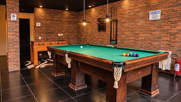 A billiards table with a green felt surface, surrounded by a brick wall and a wooden table with a netted pocket.