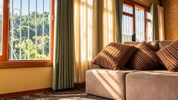 Quarto com sofá, cortinas e vista para o verde lá fora.