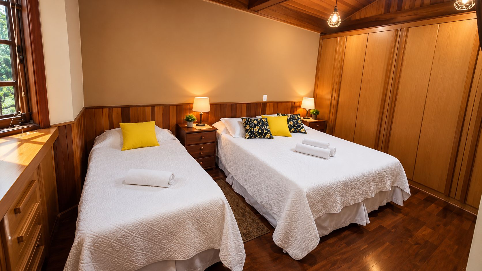 Habitación de hotel con dos camas individuales, paneles de madera, una mesita de noche con lámparas y un armario de madera.