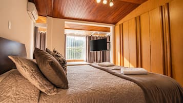 Ein Schlafzimmer mit einem großen Bett, einem Flachbildfernseher, Holzvertäfelung und einem Fenster mit Vorhängen.
