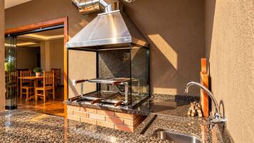 An outdoor kitchen with a grill, a sink, and a dining area with chairs and a table.