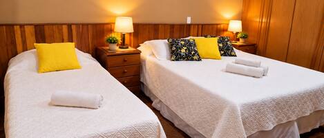 Two single beds with white linens, a wooden headboard, bedside tables with lamps, and a small potted plant.