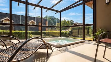A glass-enclosed outdoor area with a hot tub, wicker chairs, and a view of a residential neighborhood.