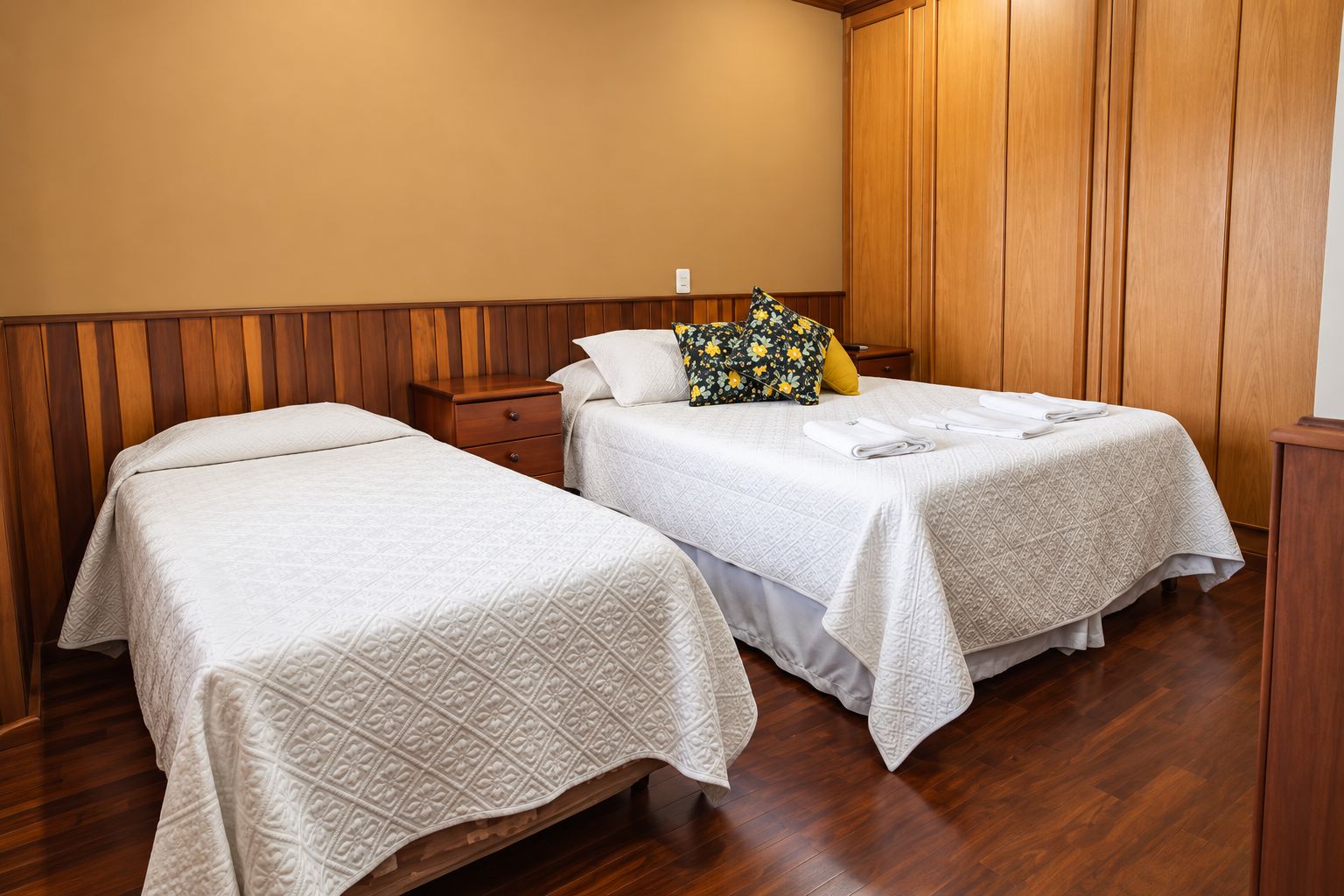 A hotel room with two beds, wooden paneling on the walls, and a wooden floor.