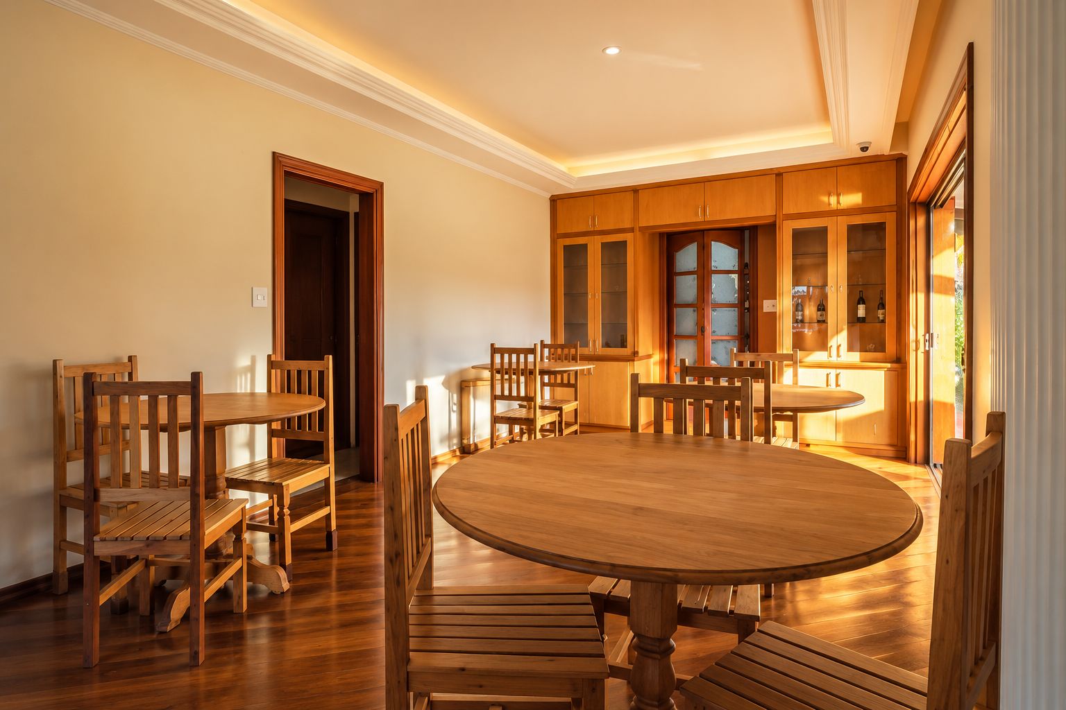 A dining area with a round wooden table and chairs, wooden cabinets, and a view of the outdoors.