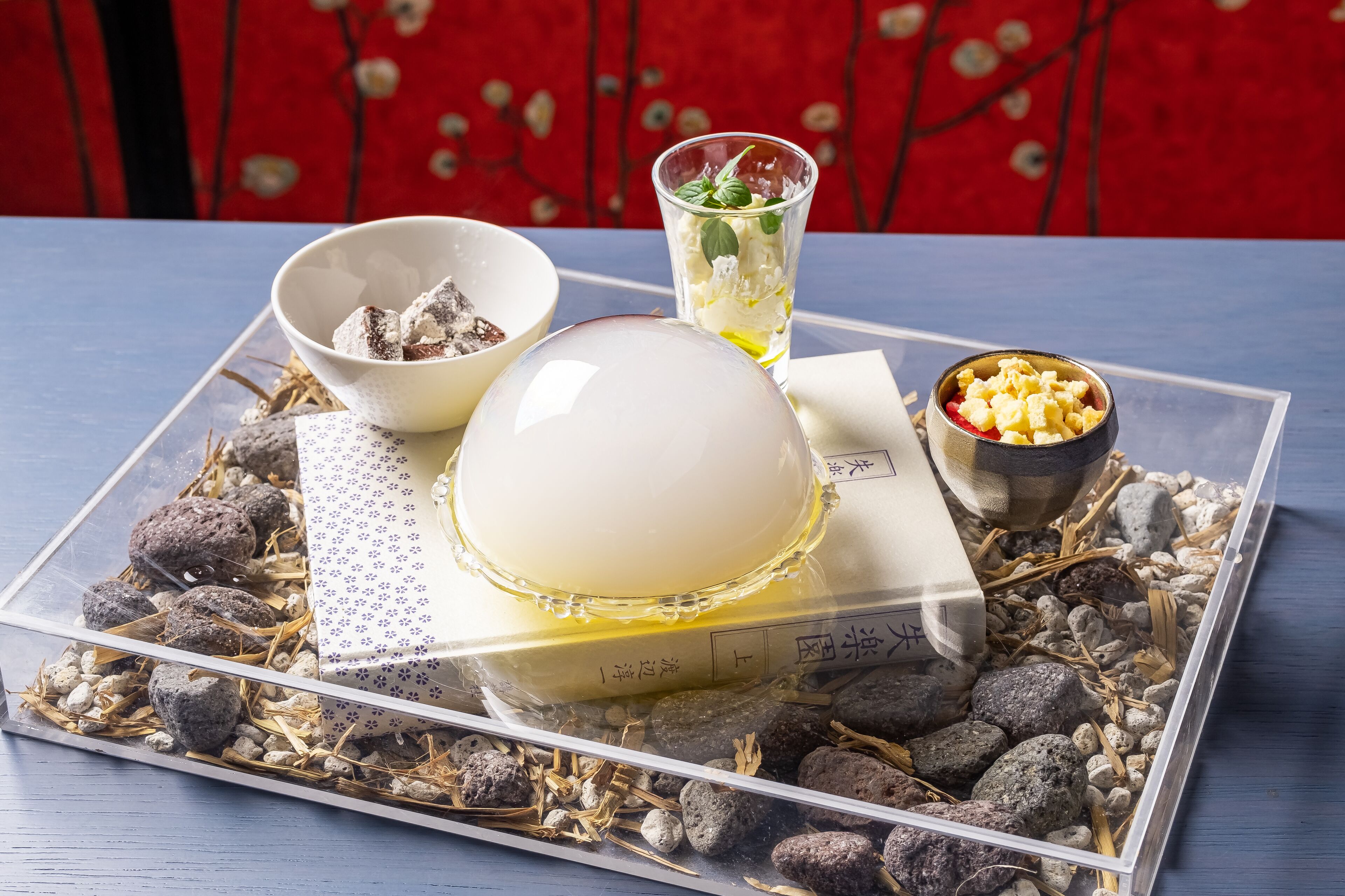 A tray with a glass of tea, a bowl of snacks, and a decorative item on a table with a red patterned background.