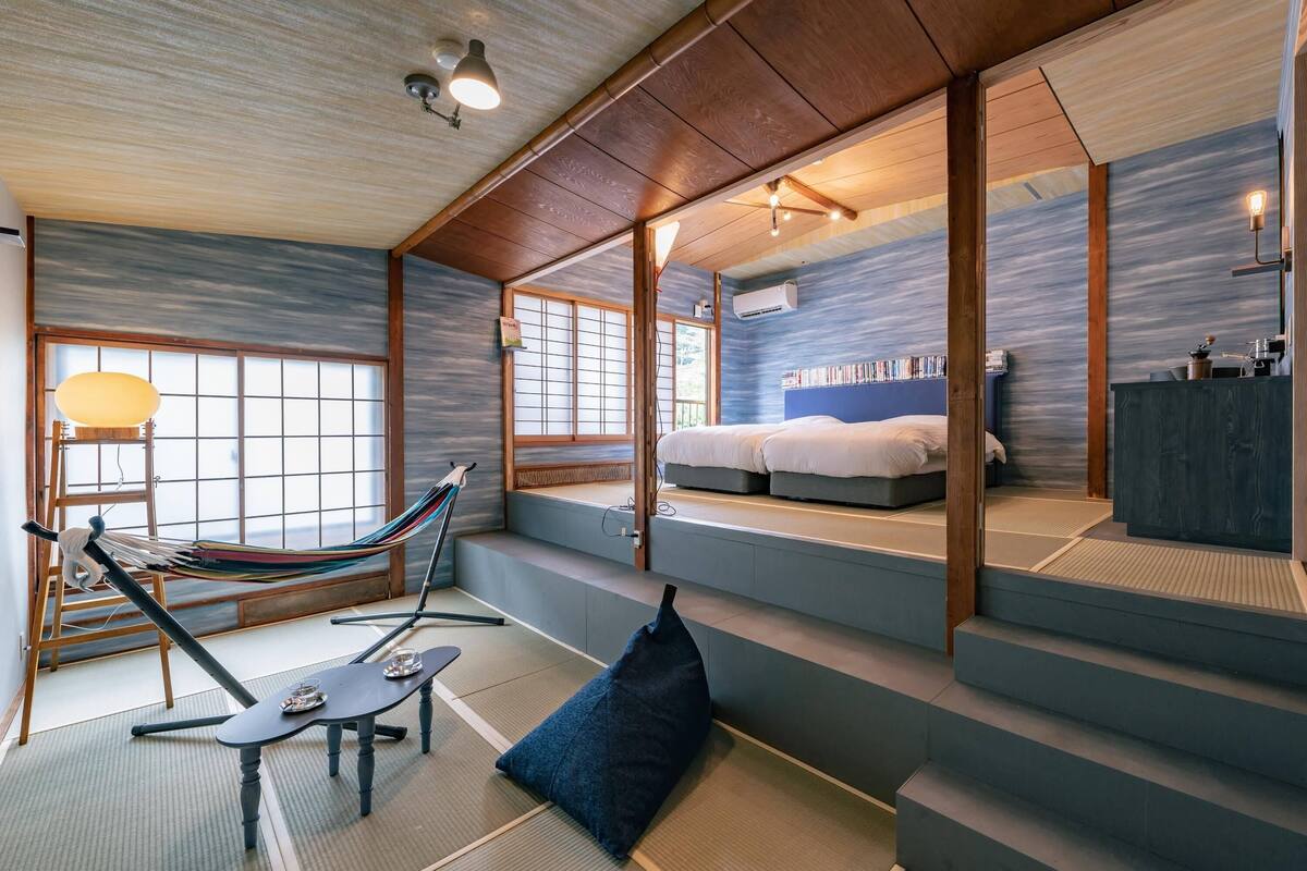 A traditional Japanese-style room with tatami flooring, a futon bed, a hammock, and a bookshelf.