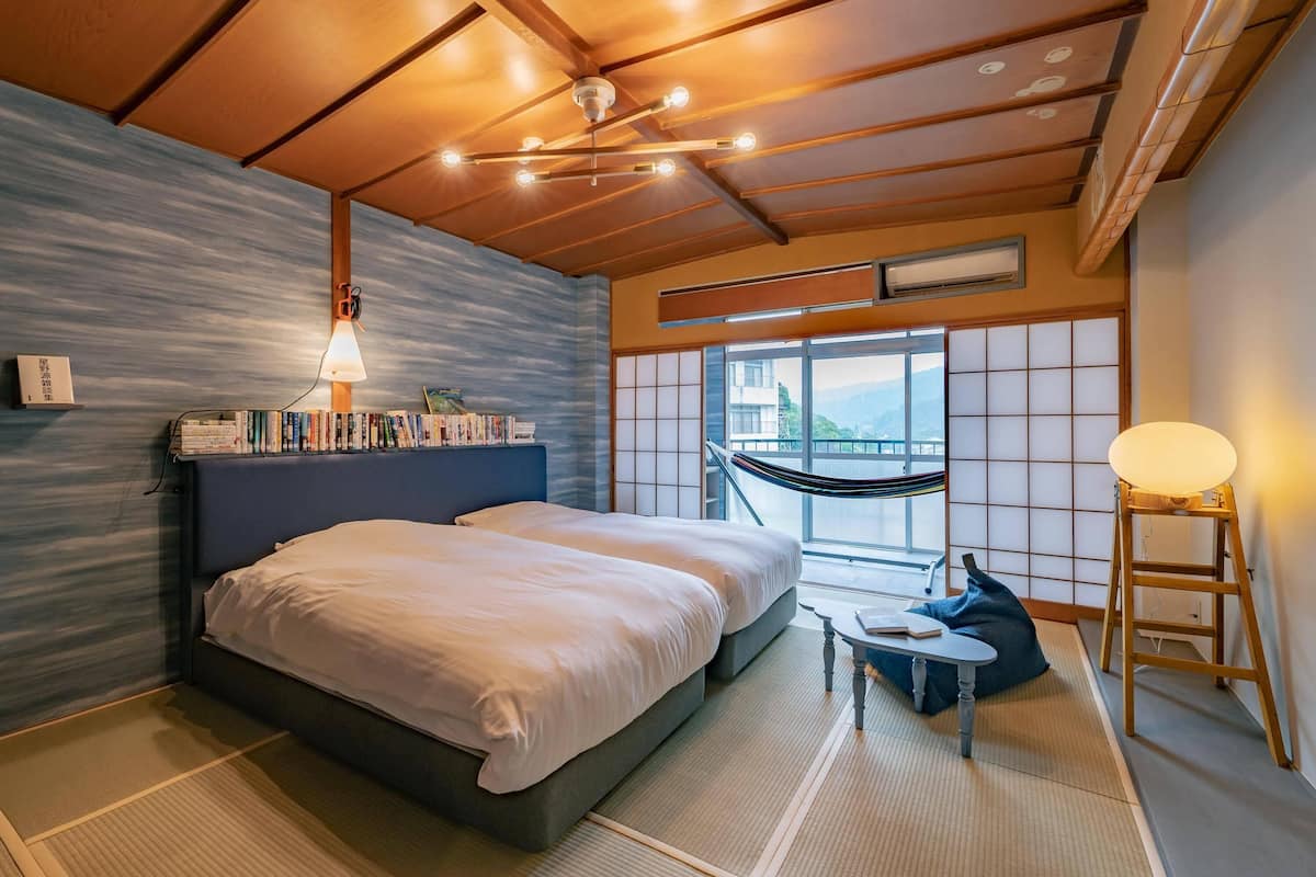 A modern hotel room with a large bed, a small table, a reading lamp, and a view of the mountains through the window.