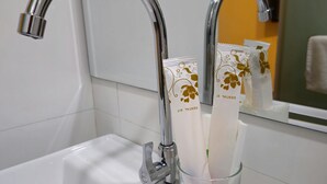 A bathroom sink with two toothbrushes in a glass holder and a mirror reflecting the bathroom. - Hotel Fortune (Johor Bahru)
