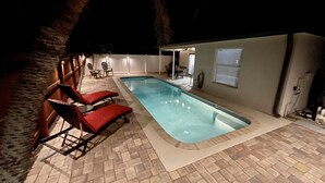 Une piscine avec deux chaises longues rouges et une terrasse en briques.