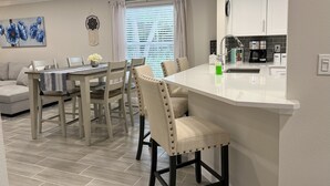 Une cuisine moderne avec des armoires blanches, un îlot central intégré et un coin repas comprenant une table et des chaises.
