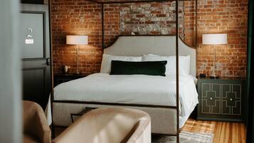 A bedroom with a four-poster bed, two bedside lamps, a wooden floor, and a brick wall.