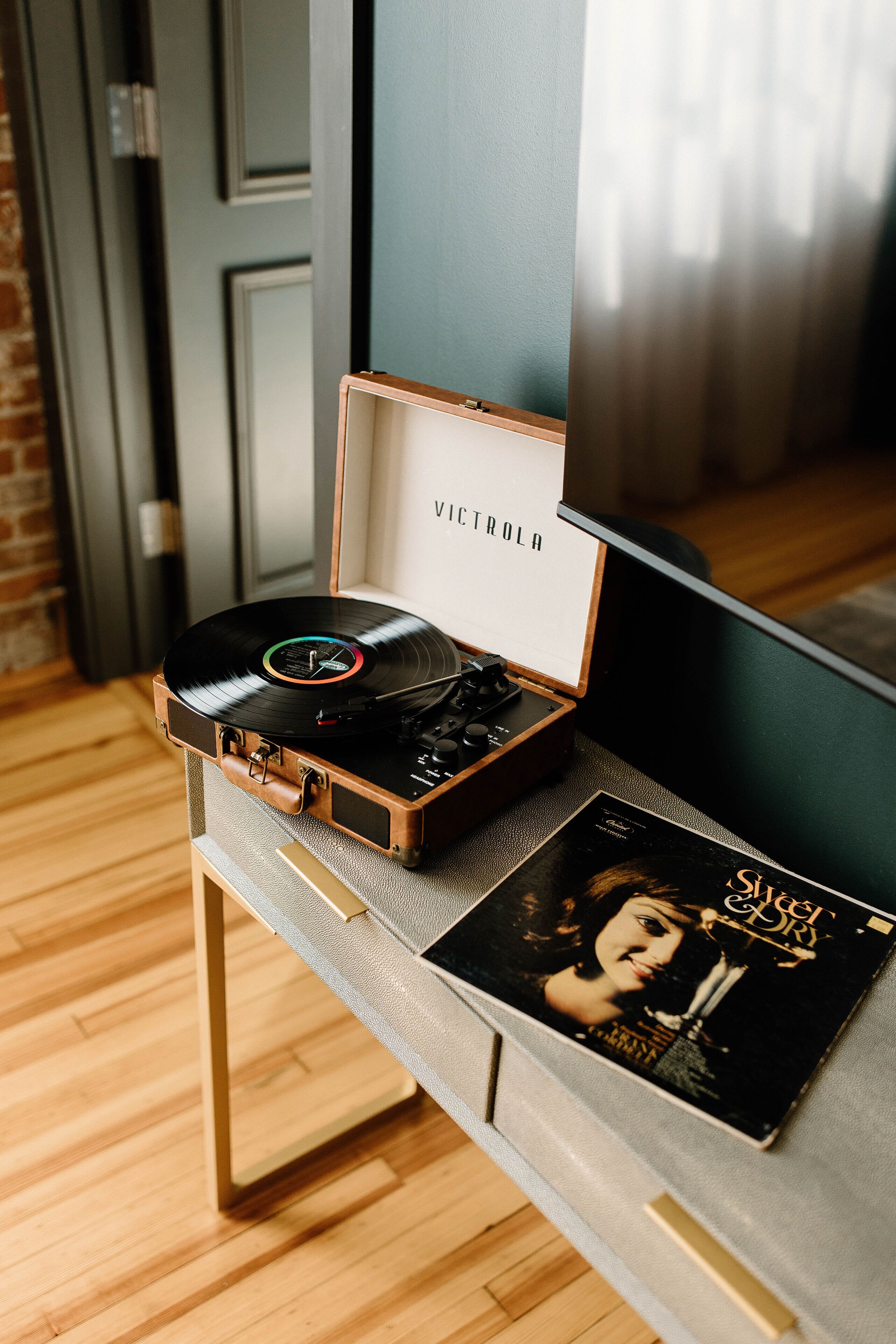 A vinyl record player in a wooden case on a table with a record sleeve beside it.