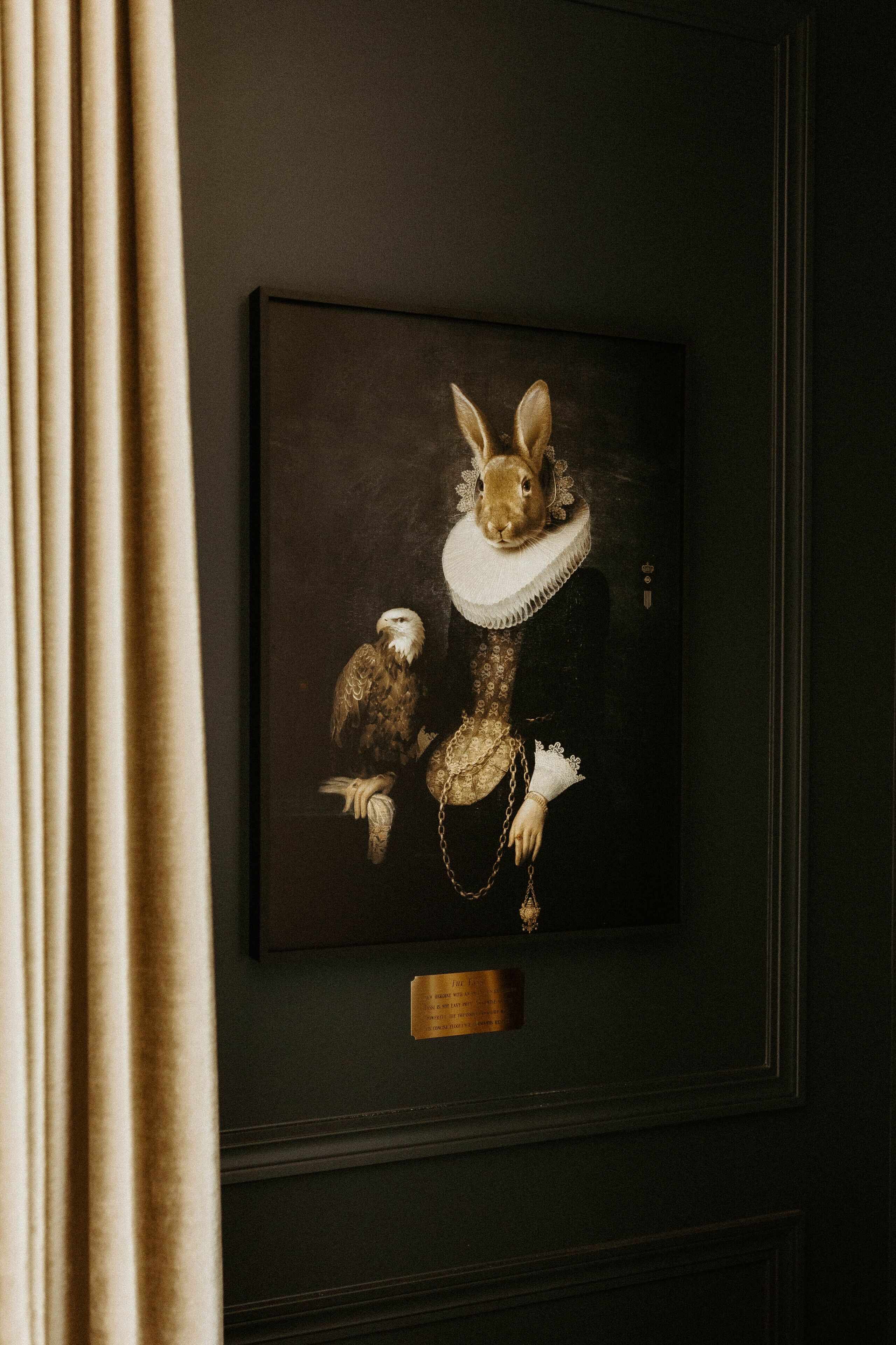 A framed artwork of a rabbit in a dress with an eagle and a chain.