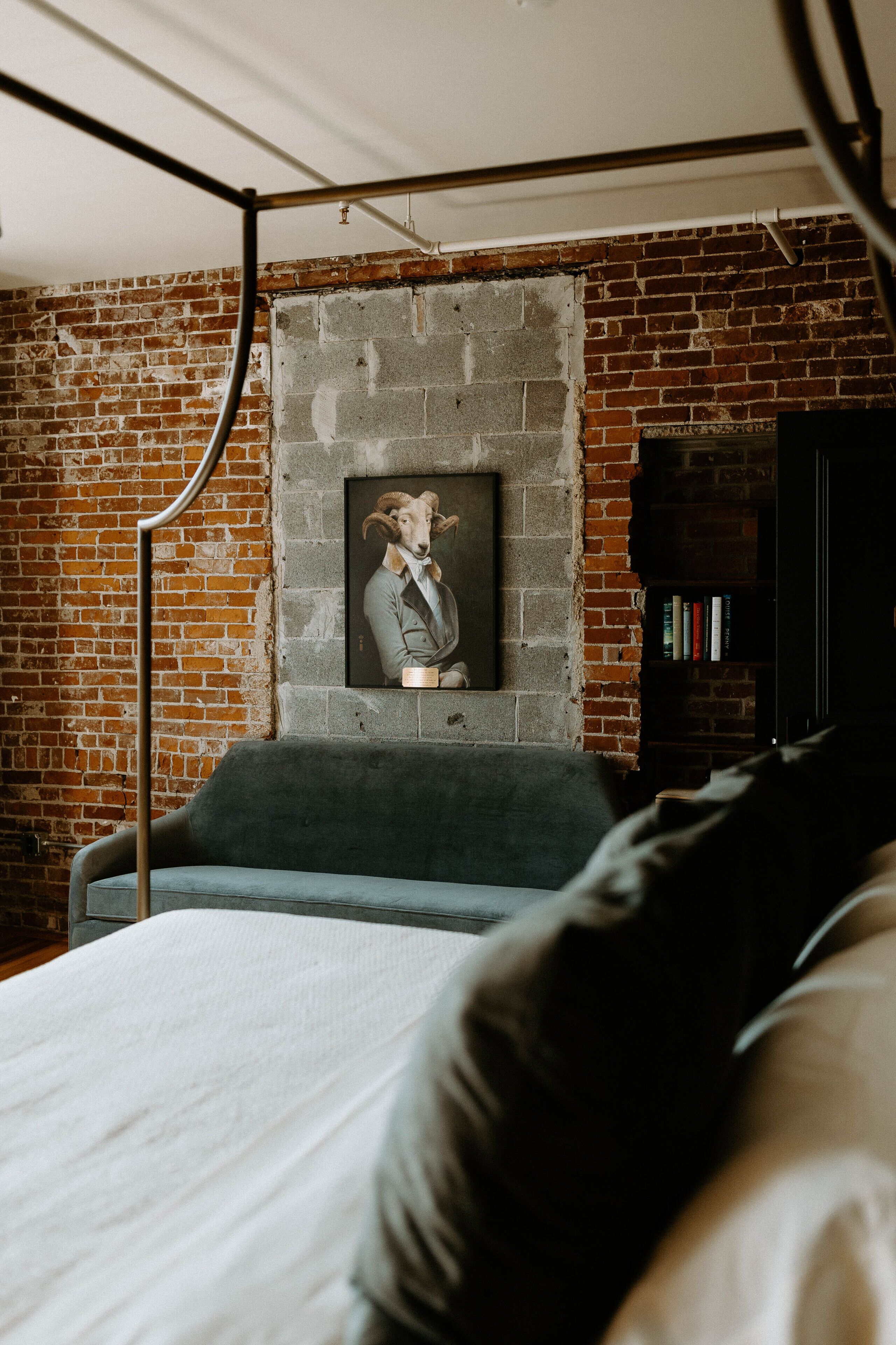 Une pièce avec un mur en briques, un canapé gris, une bibliothèque noire et un tableau encadré accroché au mur.