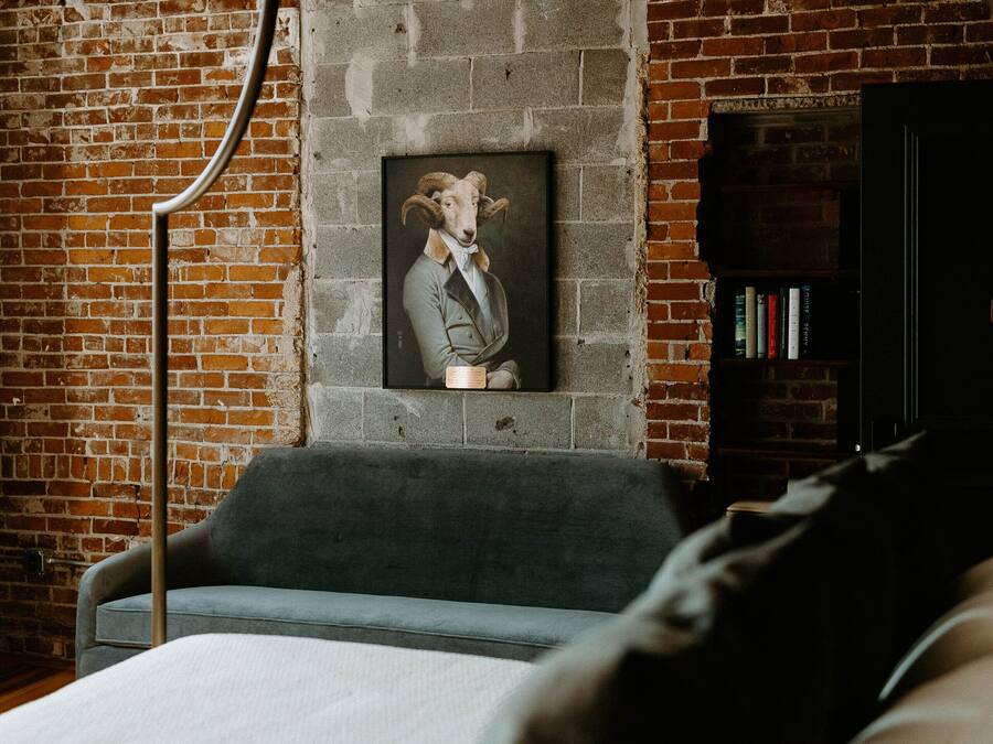 Une pièce avec un mur en briques, un canapé gris, une bibliothèque noire et un tableau encadré accroché au mur.