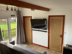 A room with a TV mounted on a wall, a wooden door, a glass door leading to a balcony, and a bed with a quilted cover.
